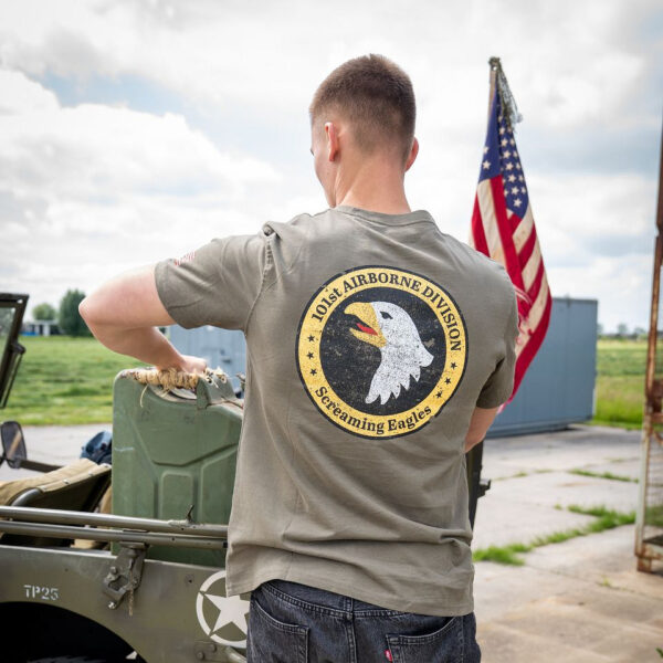 133657 11 05 Het T-shirt 101st Airborne Roundel is gemaakt van 100% BCI katoen en biedt een comfortabele en zachte draagervaring dankzij de peach finish. Met een zware kwaliteit van 170 g/m² is dit T-shirt perfect voor zowel dagelijks gebruik als outdoor activiteiten. Het is voorzien van een opvallende airborne tekstprint op de linkerborst en een grote print op de achterkant. Verkrijgbaar in een stijlvolle groene kleur, is dit T-shirt een must-have voor elke militair of outdoor liefhebber.